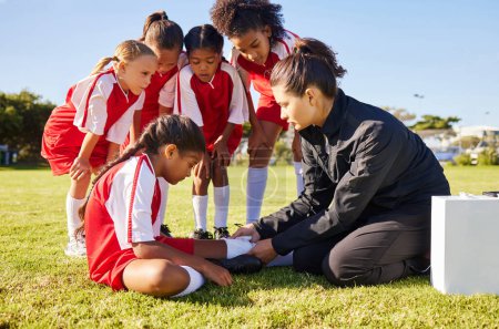 Sports, injury and children soccer team with their coach in a huddle helping a girl athlete. Fitness, training and kid with a sore, pain or muscle sprain after a match on an outdoor football field