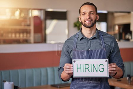 Foto de Recruitment, portrait or man with a hiring sign for job vacancy offer in cafe or small business store. Hospitality, labour shortage or happy entrepreneur smile with an onboarding message to hire. - Imagen libre de derechos