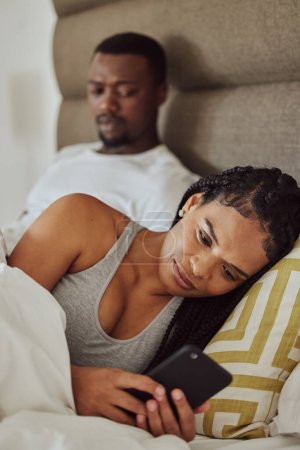 Téléchargez les photos : Couple in bed, black woman with smartphone and nosy man, cheating and suspicion for affair, unfaithful and infidelity. Partners in bedroom, male and female with cellphone, chatting and jealous guy. - en image libre de droit