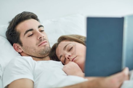 Foto de Simple pleasures mean the most. a young couple reading a book in bed while his wife sleeps on his chest at home - Imagen libre de derechos