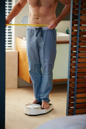 Photo for Getting closer to his goal weight. a young man weighing himself on a scale in his bathroom - Royalty Free Image