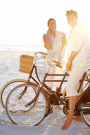 Téléchargez les photos : Biking on the beach together. A mature couple enjoying a bike ride on the beach together - en image libre de droit