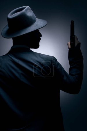 Gangster, silhouette or holding gun on studio background in secret spy, isolated mafia leadership or crime security. Model, man or dark hitman and weapon suit, fashion clothes or bodyguard aesthetic.