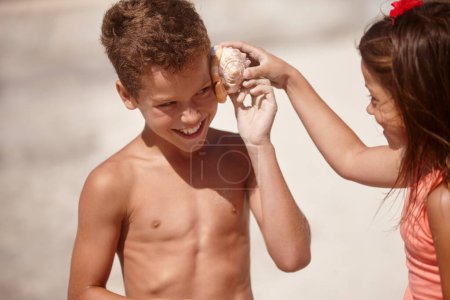 Photo for Sounds of the sea. a little girl holding a conch shell against her brothers ear - Royalty Free Image