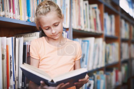 Stimulating her imagination. A cute young girl reading a book in the library