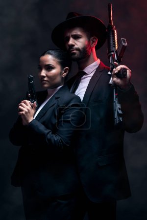 Téléchargez les photos : Gangster couple, fashion or gun on studio background in secret spy, isolated mafia safety or crime lord security. Man, love or model woman with pistol in stylish, trendy or fashion clothes aesthetic. - en image libre de droit