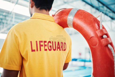 Lifeguard, man and swimming pool safety at indoor facility for training, swim and exercise. Pool, attendant and water sports worker watching for danger, protection or diving athletics, ready and safe.
