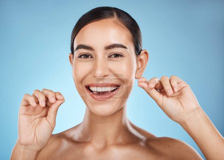 Téléchargez les photos : Woman, flossing in portrait and smile, dental healthcare for fresh breath and clean teeth isolated on blue background. Face, hands and flossing with oral hygiene product and healthy gums in studio. - en image libre de droit