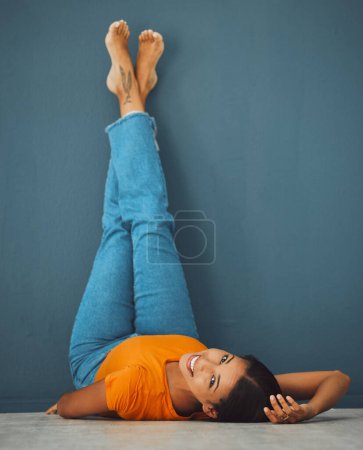 Photo for Woman on floor, smile on face with legs up on wall background and creative pose in studio. Teal copy space, young model laying on ground, portrait of happy person alone and body relaxing aesthetic. - Royalty Free Image