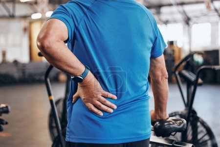 Sports, gym and old man with hand on back pain, emergency during workout at fitness studio. Health, wellness and inflammation, zoom on senior person hands on muscle cramps while training or exercise
