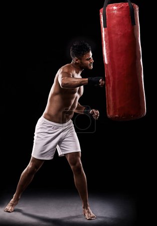 Photo for I dont need a weapon...I am one. Studio shot of kick boxer working out with a punching bag against a black background - Royalty Free Image