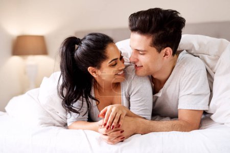 Téléchargez les photos : Bedroom, love and interracial couple together in home holding hands at night. Smile diversity and marriage of an Indian woman and man with love, care and relax happiness with a smile in a house. - en image libre de droit