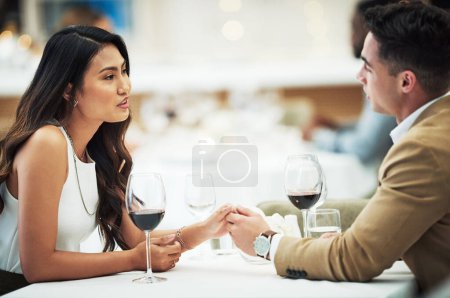 Couple, wine and holding hands in restaurant with talk, love and romance for valentines day date in night. Man, asian woman and conversation for bonding, luxury fine dining and romantic celebration.