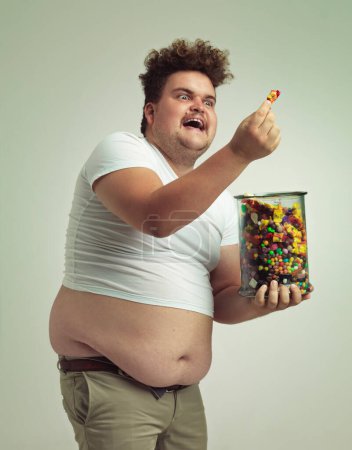 Téléchargez les photos : He has made the discovery of the century. an overweight man admiring a piece of candy - en image libre de droit