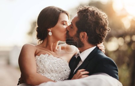 Foto de Love, wedding and kiss with a couple outdoor on their marriage day together for romance or tradition. Event, celebration or married with a birde and groom kissing outside after their ceremony. - Imagen libre de derechos