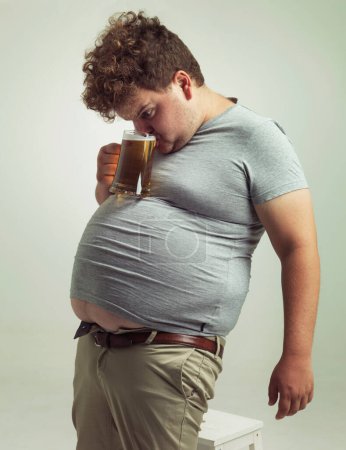 Photo for This makes drinking so much easier. an overweight man sipping a beer while it balances on his stomach - Royalty Free Image