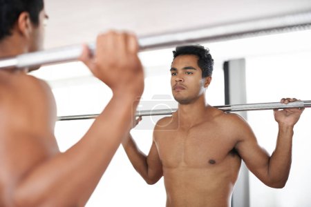 Photo for My body is a masterpiece. An athletic young man holding up a barbell while looking in the mirror - Royalty Free Image