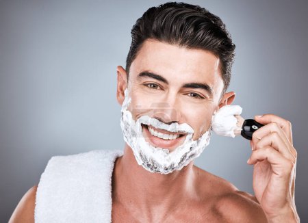 Téléchargez les photos : Face, shaving cream and man with brush in studio isolated on gray background for hair removal. Haircare portrait, epilation and happy male model with facial product, foam or gel to shave for wellness. - en image libre de droit