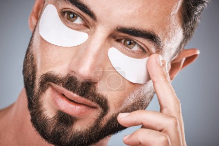 Photo for Face, man and skincare eye patches in studio isolated on a gray background for wellness. Thinking, beauty dermatology and male model apply eyes mask, cosmetics or facial treatment for healthy skin - Royalty Free Image
