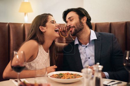 Foto de Cita, risas y pareja juguetona comiendo espaguetis en una cena romántica en un restaurante y disfrutando de una comida. Amantes, hombres y mujeres juguetones con pasta, comida o una comida el día de San Valentín y enamorados. - Imagen libre de derechos