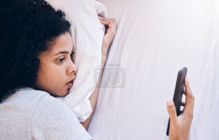Foto de Teléfono, depresión y mujer acostada en su cama mientras ve videos en las redes sociales o en Internet. Mujer cansada, somnolienta y deprimida con insomnio en red en un teléfono celular en su dormitorio en casa - Imagen libre de derechos