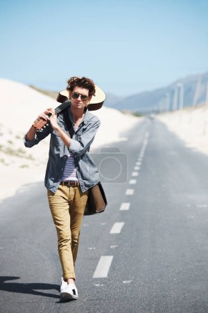 Photo for I have to get to that gig. Trendy young man holding his guitar over his shoulder walking down the road - Royalty Free Image