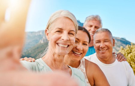 Foto de POV of a group of active seniors posing together for a selfie or video call on a sunny day against a mountain view background. Happy retirees exercising together outdoors. Living healthy and active l. - Imagen libre de derechos