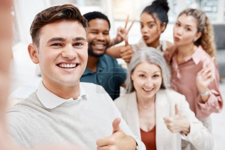 Photo for Group of cheerful diverse businesspeople taking a selfie together at work. Happy caucasian businessman showing a thumbs up while taking a photo with his content colleagues. - Royalty Free Image