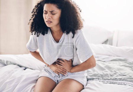 Téléchargez les photos : Abdomen pain, period and black woman in bed with abdominal cramps, menstruation and stomach ache. Health, medical emergency and girl with digestion problem, pms crisis and endometriosis in bedroom. - en image libre de droit