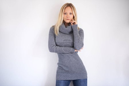 Foto de Confident shell hit the style mark this winter. Confident young woman dressed in warm winter clothing posing against a grey background - Imagen libre de derechos