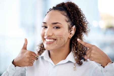 Thumbs up, happy and portrait of a woman with a hearing aid pointing to her ear in the office. Happiness, success and young professional female with a deaf piece and a approval gesture in workplace