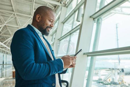 Photo for Black man, phone and chatting at airport for business travel, trip or communication waiting for flight. African American male smile for conversation, schedule or checking plain times on smartphone. - Royalty Free Image