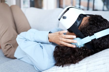 Téléchargez les photos : Virtual reality, metaverse and gaming with a black woman on a sofa in the living room of her home. AI, 3D and VR with a young female gamer using a headset to access cyberspace for a video game. - en image libre de droit