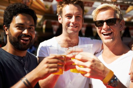 Téléchargez les photos : À la tienne. Trois jeunes hommes trinquent leurs bières lors d'un festival de musique - en image libre de droit