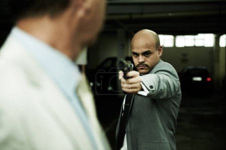 Photo for Move and youre dead. A criminal aiming his handgun at a surprised executive in a dark parkade - Royalty Free Image