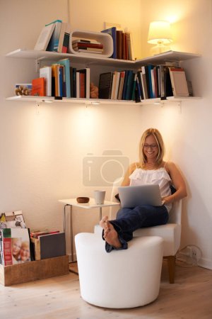 Foto de Enjoying a relaxing day at home. Attractive young woman using her laptop in an armchair at home - Imagen libre de derechos
