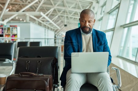 Photo for Black man, laptop and luggage at airport for business travel, trip or working while waiting to board plane. African American male at work on computer checking online schedule times for flight delay. - Royalty Free Image