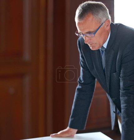 Téléchargez les photos : Contemplating his next move. Close-up shot of a senior businessman standing in his office leaning over his desk - en image libre de droit