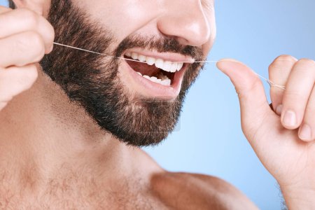 Téléchargez les photos : Dental, floss and oral hygiene with a man in studio on a blue background cleaning his teeth for healthy gums. Dentist, healthcare and mouth with a young male flossing to remove plague or gingivitis. - en image libre de droit