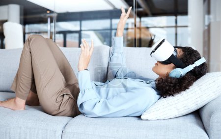 Téléchargez les photos : Virtual reality, metaverse and gamer with a black woman on a sofa in the living room of her home. AI, 3D and VR with a young female gaming using a headset to access cyberspace for a video game. - en image libre de droit
