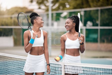Photo for Friends bonding after a tennis match. African american woman talking after a game of tennis. Young women walking and talking on the tennis court. Carefree girls walking by the net on the tennis court. - Royalty Free Image