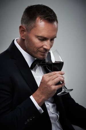 Téléchargez les photos : Tuxedo, wine glass and man with alcohol in a suit feeling classy with a luxury drink. Gray background, isolated and studio with a model, agent or actor with a glass to smell rich wines with mockup. - en image libre de droit