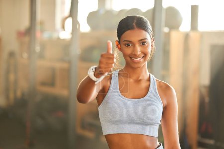Téléchargez les photos : Votre jeu de fitness devient bon. Portrait d'une jeune femme en forme montrant les pouces dans une salle de gym - en image libre de droit