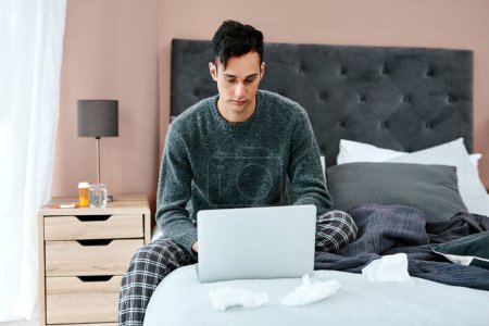 Photo pour Feeling well enough to work from home. a young man using a laptop while recovering from an illness in bed at home - image libre de droit
