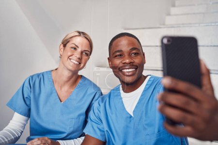 Téléchargez les photos : Healthcare, selfie and staff with happiness, hospital and celebrate achievement, interns and cheerful together. Medical professionals, woman and black man with smartphone, taking pictures and joyful. - en image libre de droit