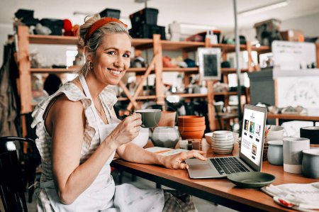 Photo for Coffee and technology are 21st century necessities. Cropped portrait of an attractive mature woman sitting alone and using her laptop in her pottery workshop while drinking coffee - Royalty Free Image
