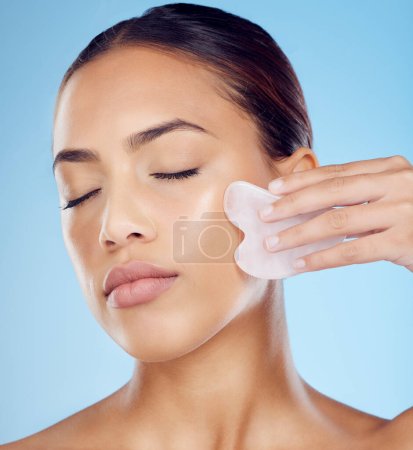 Téléchargez les photos : Woman, beauty and face massage with gua sha, facial product or aesthetic skincare in studio. Young model, crystal stone tools and wellness for natural cosmetics, rose quartz dermatology or body salon. - en image libre de droit