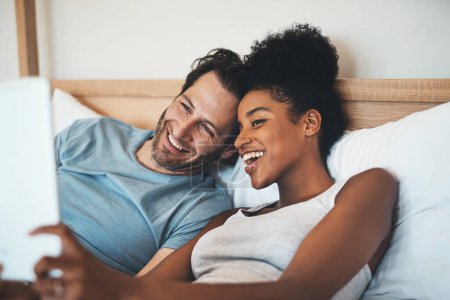 Téléchargez les photos : Hey there fam. an affectionate young couple video calling using a digital tablet in bed in the morning - en image libre de droit