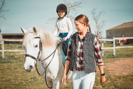 .Frau, Kind auf dem Pferd und glücklicher Ranch-Lebensstil und Tier, das mit Mädchen, Mutter und Lächeln auf dem Feld spaziert. Land, ländliche Natur und Nutztiere, Mutti unterrichtet und hilft Kind beim Ponyreiten in den USA