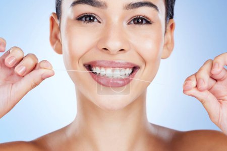 Téléchargez les photos : Face, flossing teeth and dental with woman, hygiene and beauty with grooming and mouth care on blue background. Hands, string and healthy gums with fresh breath, health and skin glow in portrait. - en image libre de droit